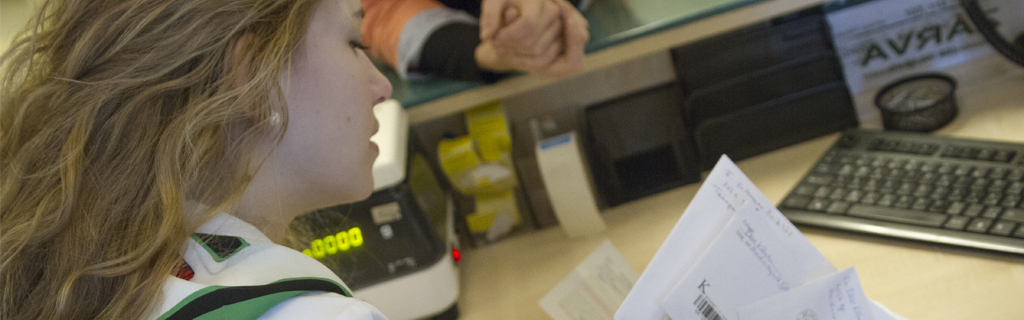 A képen egy postai ügyintéző hölgy látható kezében sok levéllel.