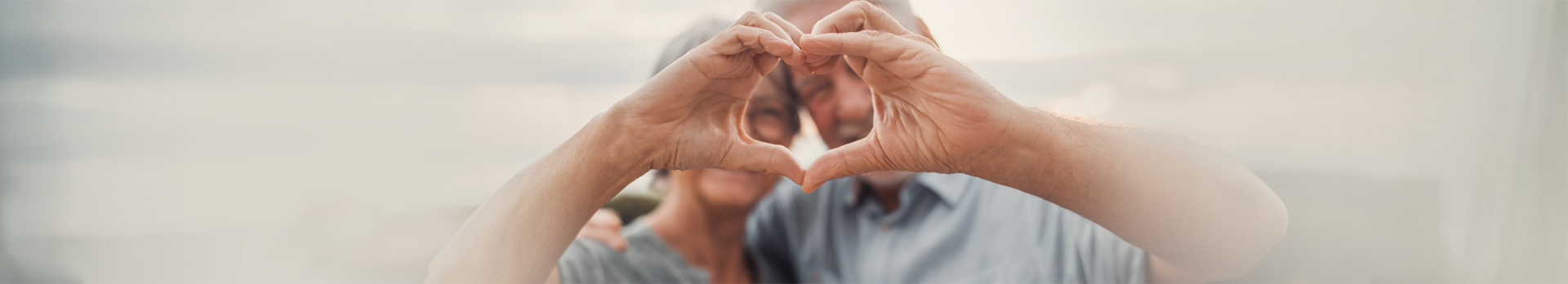 Idősödő házaspár, kezükkel szivet formáznak.